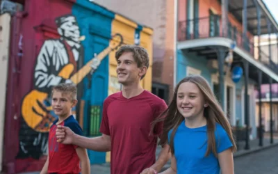 Three kids walk arm in arm down a street with colorful murals. One mural features a musician with a guitar. The buildings have balconies and vibrant facades, creating a lively, artistic atmosphere. "Things to Do in Orleans With Kids"