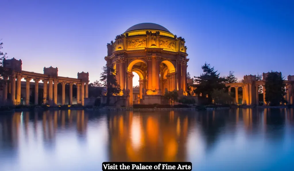 The illuminated Palace of Fine Arts in San Francisco is reflected in a tranquil pond at twilight, surrounded by trees and classical columns, with a text banner at the bottom.
