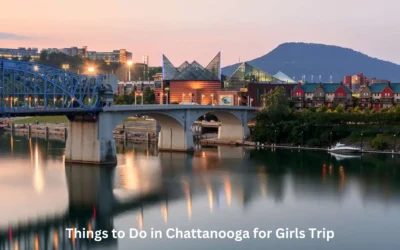 Cityscape of Chattanooga at dusk, featuring a river with a lit bridge and modern buildings in the background. Text overlay reads, Things to Do in Chattanooga for Girls Trip.