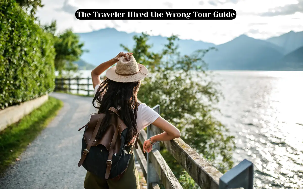 A person with a backpack and hat stands on a path by a lake, looking at the scenic view of mountains and water under a cloudy sky. A caption reads, The Traveler Hired the Wrong Tour Guide.